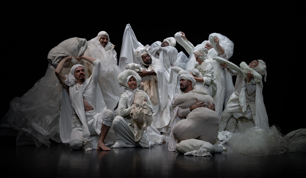 Gruppo di danzatori vestiti di bianco e ricoperti di teli e plastiche nella pi